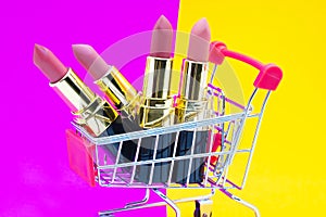 Colorful pink Lipstick in a red shopping cart on orange and yellow background,beauty and shopping concept,selective focus