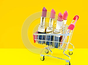 Colorful pink Lipstick in a red shopping cart on orange and yellow background,beauty and shopping concept,selective focus