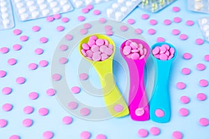 Colorful pink tablets in colored plastic round spoons. Blisters of pills in the background. Concept of medicine