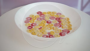 Colorful pink, yellow crispy corn rings in white plate with milk rotating on kitchen background. Delicious breakfast