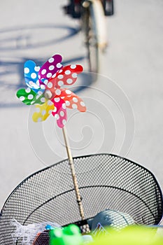 Colorful pinwheel attached to bicycle basket to entertain toddler child riding on front child seat on bike in summer.