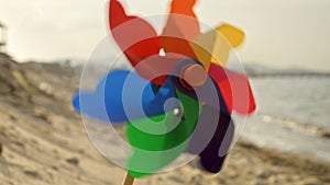 Colorful pinwheel spins joyfully on a sandy beach. Nostalgia of childhood summers, beach tourism, and the pursuit of happiness