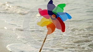 Colorful pinwheel spins on a sandy beach next to rolling sea waves, joy of travel, exploration, and the pursuit of happiness and