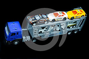 colorful plastic car carrier truck, deep blue gray truk with deep gray white yellow toy cars on black back ground.