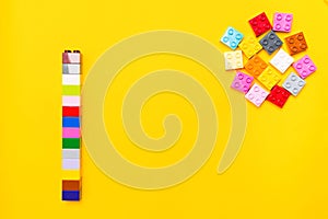 Colorful plastic construction of square block elements of toy constructor with separate bricks on yellow background with copy