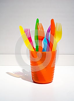 Colorful plastic forks and knives in orange plastic cup