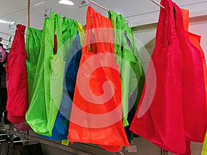 Colorful plastic shopping bags hang on supermarket shelf.