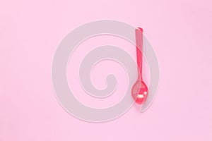 Colorful plastic spoon on pink table background with co