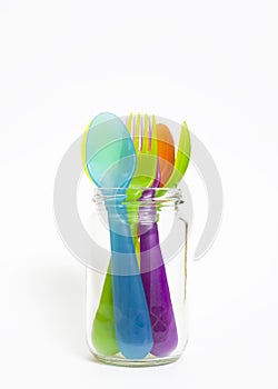 Colorful plastic spoons and forks in jar .