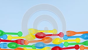 Colorful plastic spoons and forks ordering on bottom of blue background - Stop motion