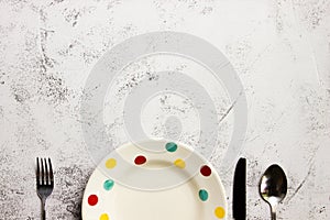 A colorful plate with fork and spoon on grey background.