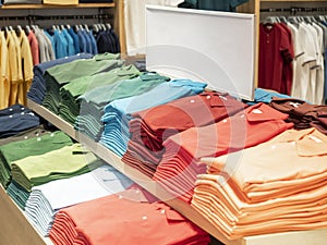 Colorful polo t shirt stack on shelf in large department store shop. Copy space on white sign board.