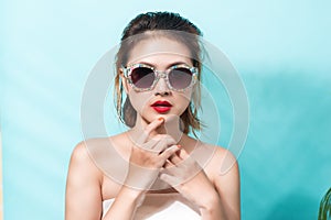 Colorful portrait of young attractive asian woman wearing sunglasses on blue. Summer beauty concept.