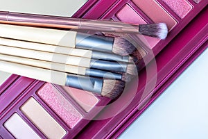 Colorful professional eye shadow palette in pink colors and a set of makeup brushes on it. Color palette