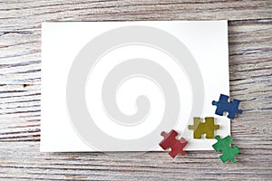 Colorful puzzles on white wooden background with white paper sheets, frame, early childhood autism concept, mocap, copy