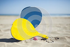Colorful rackets and a ball in the sand of the beach in a sunny