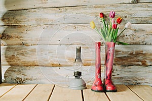 Colorful rain boots with spring flowers and oli lamp in wooden b