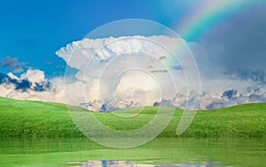 Colorful rainbow above green hills, blue sky with white incus cl
