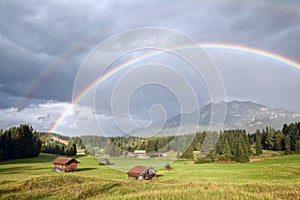 Colorful rainbow over alpine meadows with wooden huts
