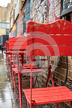 Colorful red chairs in the streets of London under a light rain