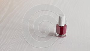 Colorful red nail polish bottle on a white wooden table. Girl puts a glass bottle on the table