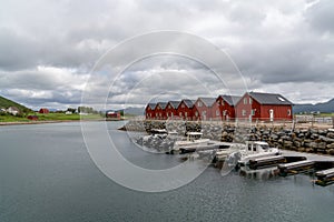 Colorful red wooden houses on the oceanfront in the Lofoten Islands of Norway with boats at the dock in the foreground