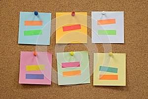 Colorful reminder sticky notes push pins on cork board.