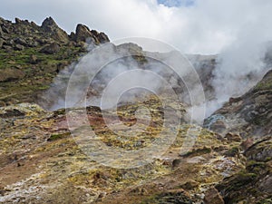 Colorful rhyolit red, orange and yellow fumarole at Reykjadalur valley with sharp rocks, grass meadow and geothermal steam. South