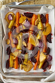 Colorful roasted vegetables on tray with parchment. Mix of carrots, beets, turnips, rutabaga, onions. Vegetarianism, veganism,