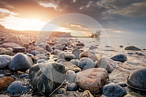 Colorful rocks of Salthill beach in focus. Blackrock diving board out of focus. Sun rise time. Sun flare and cloudy sky. Nobody.