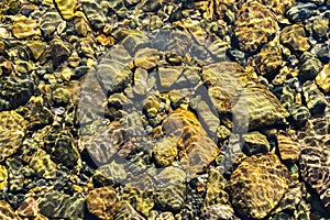 Colorful rolling stones pattern with still water. Colorful sea stones under still water. Iridescent sunlight on the stones. Transp