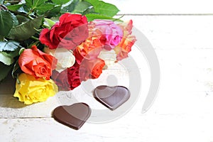 Colorful roses with chocolate hearts on white wooden boards