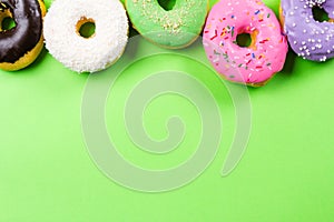 Colorful round donuts on green background. Flat lay, top view.