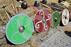 Colorful round shields, light batlle axes, conical helmets and various knives displayed on medieval summer festival