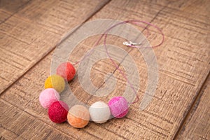 Colorful round wool felt beads necklace handmade with white, pink, red, orange and peachy color beads on a wood table