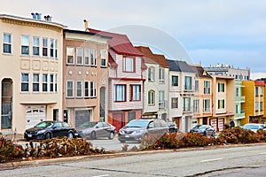 Colorful row of San Francisco houses in compact housing with vehicles on street