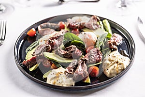 Colorful salad with flank steak filling the dark plate on a restaurant table