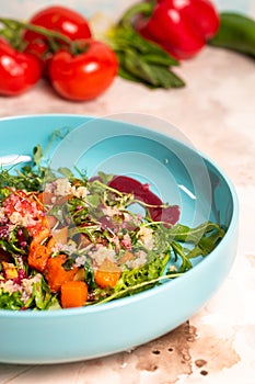 Colorful salad with pumpkin, lettuce, tomatoes, and quinoa on a blue plate