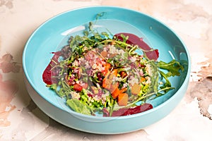 Colorful salad with pumpkin, lettuce, tomatoes, and quinoa on a blue plate