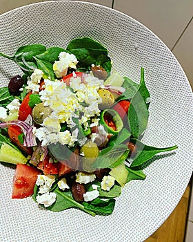 colorful salad, sliced cucumbers and tomatoes, black olives, green olives, baby spinach leaves, crumbled feta cheese, olive oil