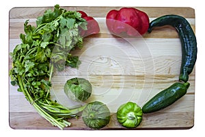 Colorful salsa frame - Cutting board with cilantro and tomatillos and assorted hot and sweet peppers arranged around the sides and