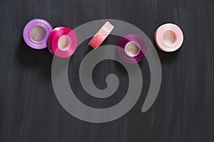 A colorful satin ribbon in a rolls on a chalkboard table, with abstract dark background and copy space.