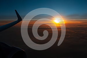 Colorful scenic view of beautiful dark sunset, cloudy sky and airplane wing with engine, through window of the aircraft.