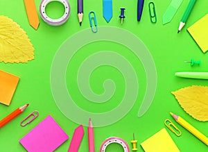 Colorful school items with autumn leaves as a frame on green background