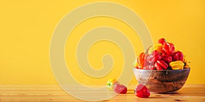 Colorful scotch bonnet chili peppers in wooden bowl over orange background. Copy space.