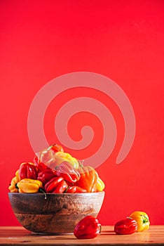 Colorful scotch bonnet chili peppers in wooden bowl over red background. Copy space.