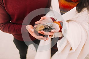 Colorful sea pebbles on couple's hands close up. Happy young couple at the winter beach wrapped in white blanket