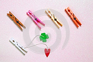 Colorful set of five wooden and plastic clothespins on a light pink glitter sparkle background with space. A red heart and a green