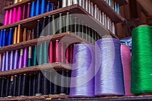 Colorful sewing thread spool arranged on wooden shelf.