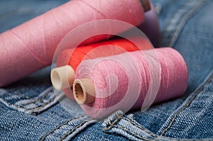 colorful sewing thread spool bobbins on blue jeans background